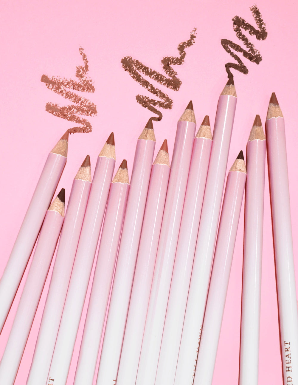 Több P.Louise Ultimate Definition Sharpenable Lip Liner képe egy csoportba rendezve, és néhány termék látható felettük rózsaszín háttéren