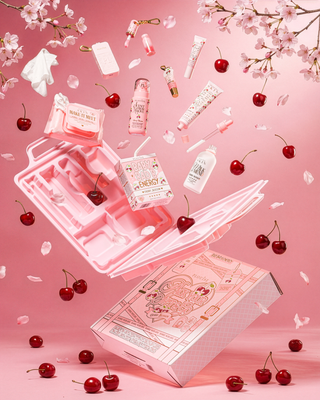 Cherry blossom skincare products floating in the air surrounded by cherries and blossoms against a pink background