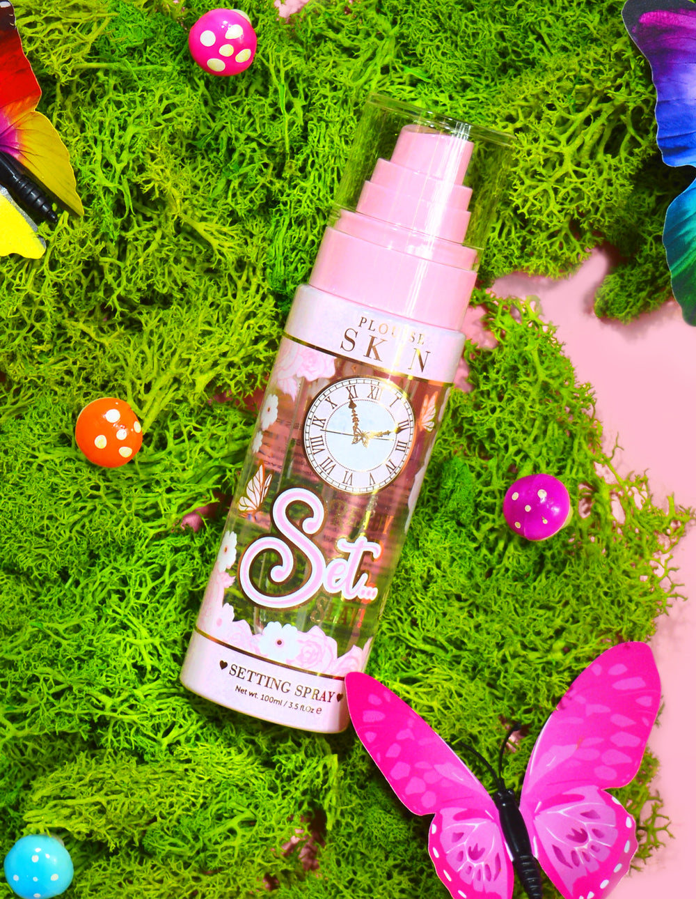 Egy üveg P. Louise Ready Set Slay Long Lasting Setting Spray dekoratív elemekkel, köztük színes műmohával, pillangókkal és gombákkal körülvéve.